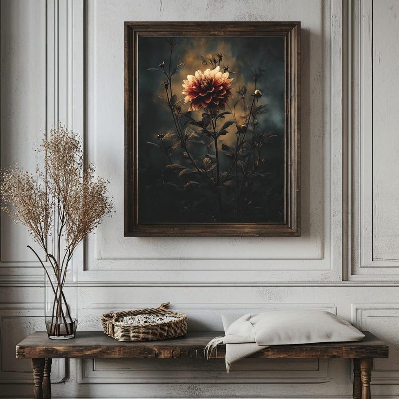 Op de afbeelding: Een ingelijste print van een rode en gele dahlia bloem, tegen een donkere achtergrond. Het kunstwerk zit in een bruine houten lijst. De print hangt boven een houten bank met een gevlochten mand en een kussen.