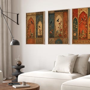 May include: Three framed wall art pieces with an ornate, vintage design. Each features a central archway with floral and architectural elements, a bird, and a color palette of red, blue, and gold. The frames are a light brown color.