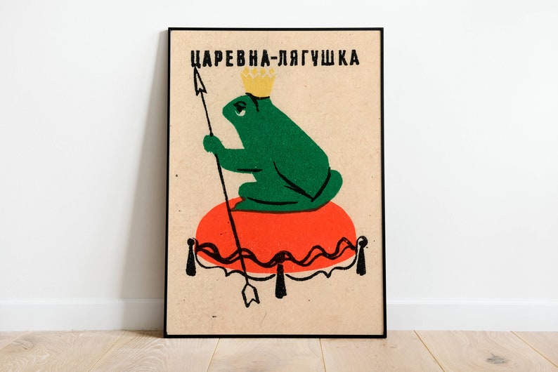 Op de afbeelding: Een vintage poster met een groene kikker die een gouden kroon draagt en op een rood kussen zit. De poster heeft de tekst "Царевна-лягушка" in zwarte letters.