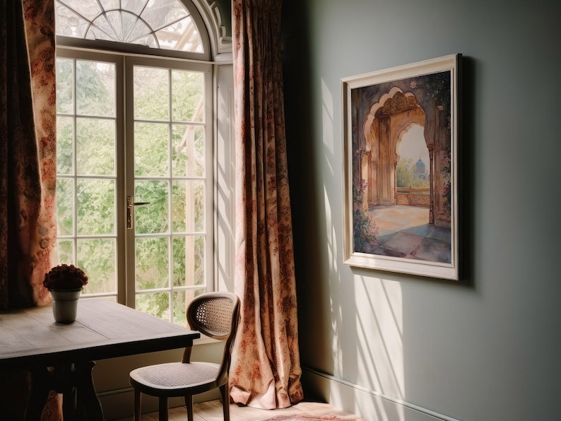 May include: A room with a large window, a table and chair, and a framed painting of an archway with a view of a garden. The walls are painted a light blue-green color and the curtains are a floral pattern in shades of pink and brown.