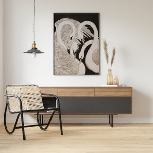 May include: A black and white illustration of three swans with their necks intertwined, framed and hanging on a white wall above a wooden dresser with black drawers.