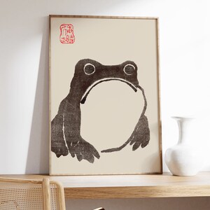 May include: A framed black and white illustration of a frog with a red stamp in the top left corner. The stamp contains Japanese characters.