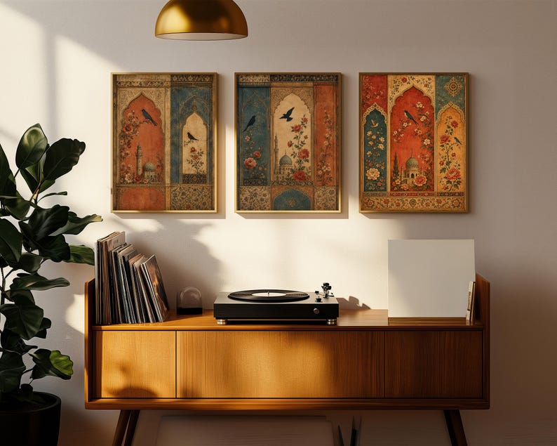May include: Three framed wall art pieces with ornate, vintage-style designs. Each features a central archway motif with birds, flowers, and architectural elements in shades of red, blue, and gold. The artwork hangs above a wooden cabinet with a record player.
