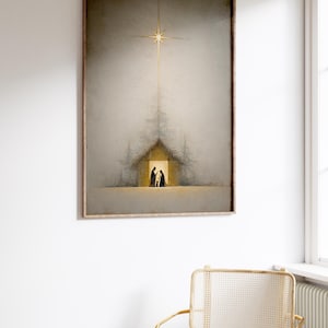 May include: Framed art print depicting a Nativity scene. The artwork features a golden star shining above a simple building with figures inside. The color palette is muted with soft grays and golds, creating a serene atmosphere. The frame is a warm, natural wood tone.