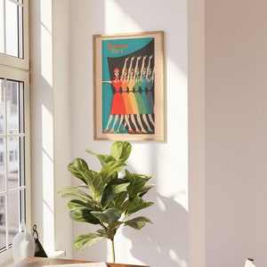 May include: A framed poster with a retro design featuring a line of women in colorful dresses dancing. The poster has a blue background with a rainbow gradient and the text "Dance More".