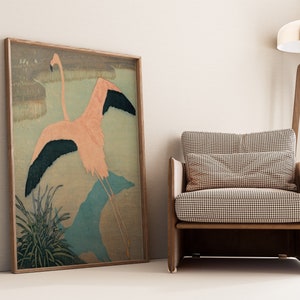 May include: A framed print of a pink flamingo with black wings in flight, set against a background of green and blue brushstrokes. The print is displayed in a living room setting with a brown armchair and a floor lamp.