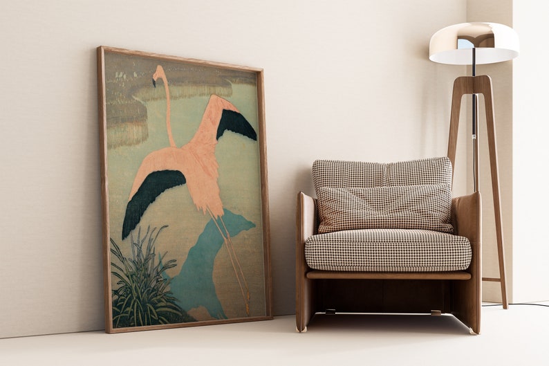 May include: A framed print of a pink flamingo with black wings in flight, set against a background of green and blue brushstrokes. The print is displayed in a living room setting with a brown armchair and a floor lamp.