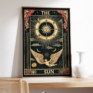 Op de afbeelding: Een zwarte en gouden tarotkaart met de afbeelding van een ge Fl&uuml;gelde engel die in de lucht vliegt. De kaart is getiteld "De Zon" en heeft een zon met een gezicht in het midden.