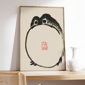 May include: A framed black and white ink painting of a frog with a red seal in the center. The seal has Chinese characters on it.