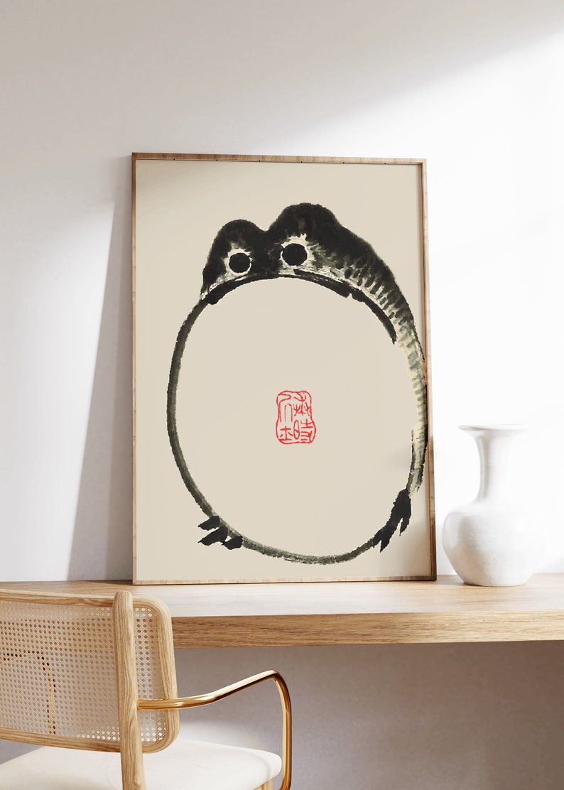 May include: A framed black and white ink painting of a frog with a red seal in the center. The seal has Chinese characters on it.
