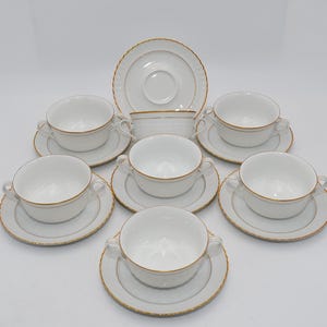 Può includere: Un set di ciotole da zuppa in porcellana bianca con finiture dorate. Il set comprende zuppiere con manici, piattini e una zuppiera da portata. Le ciotole e i piattini hanno un motivo strutturato.