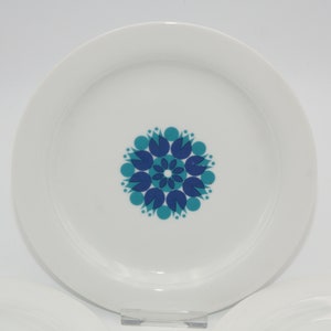 Pode incluir: Um prato de cerâmica branco com um design floral azul e turquesa. O design apresenta uma flor central com pétalos e folhas.