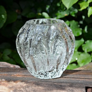 Pode incluir: Um vaso de vidro transparente com uma superfície texturizada e ondulada. O vaso tem uma forma arredondada e bulbosa.