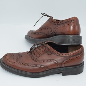 May include: A pair of brown leather brogue shoes with lace-up closures. The shoes have a wingtip design and a textured sole.