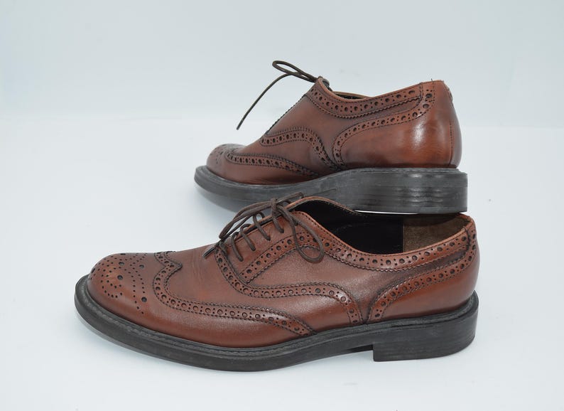 May include: A pair of brown leather brogue shoes with lace-up closures. The shoes have a wingtip design and a textured sole.