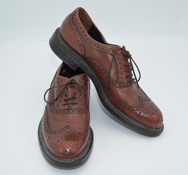 May include: A pair of brown leather brogue shoes with lace-up closures. The shoes have a wingtip design and a perforated pattern.