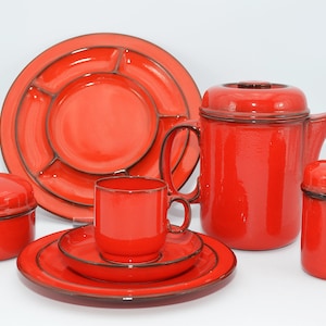 Op de afbeelding: Een rode keramische theeset met een theepot, roomkan, suikerpot, kop en schotel, en een verdeelde serveerschaal.