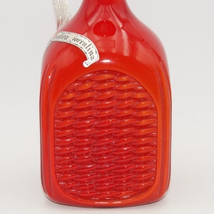 Könnte beinhalten: Rote Glasflasche mit einem gewebten Muster und einem silbernen Etikett mit der Aufschrift "Gallina "orentina".