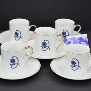 Könnte beinhalten: Set aus fünf weißen Porzellan-Teetassen und Untertassen mit einem blauen Blumendesign und goldenen Verzierungen.