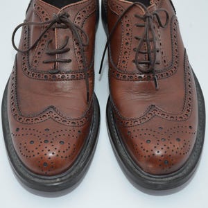 May include: A pair of brown leather brogue shoes with a lace-up closure. The shoes have a wingtip design and a perforated pattern.