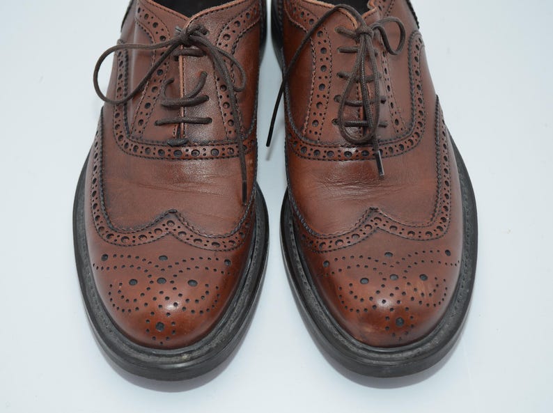 May include: A pair of brown leather brogue shoes with a lace-up closure. The shoes have a wingtip design and a perforated pattern.