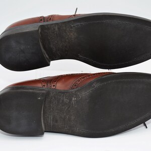 May include: A pair of brown leather shoes with a brogue design. The shoes have black soles and are shown from the bottom.
