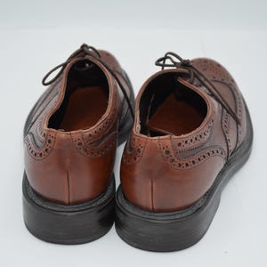 May include: A pair of brown leather brogue shoes with wingtip detailing. The shoes have a lace-up closure and a black leather sole.