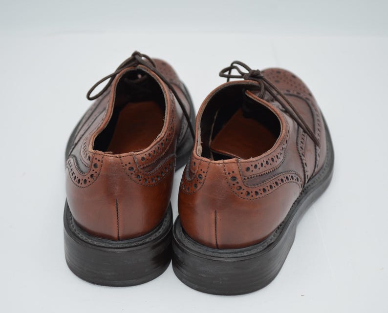 May include: A pair of brown leather brogue shoes with wingtip detailing. The shoes have a lace-up closure and a black leather sole.