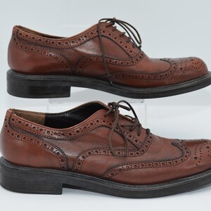May include: A pair of brown leather brogue shoes with lace-up closures. The shoes have a wingtip design and a textured sole.
