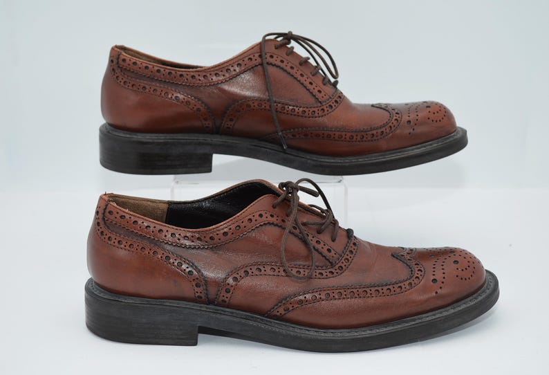May include: A pair of brown leather brogue shoes with lace-up closures. The shoes have a wingtip design and a textured sole.