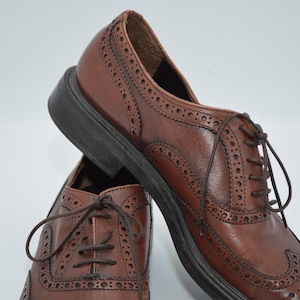 May include: A pair of brown leather brogue shoes with lace-up closures. The shoes have a wingtip design and a textured sole.