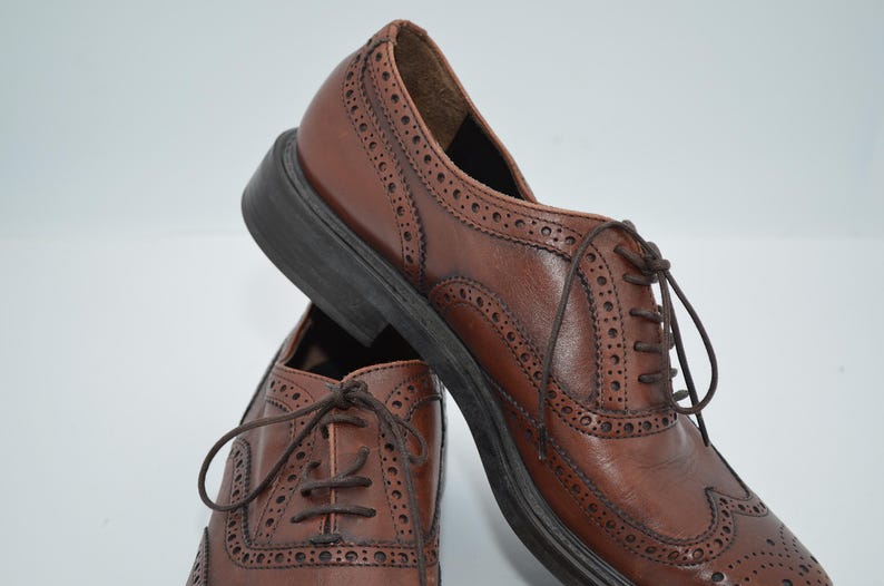 May include: A pair of brown leather brogue shoes with lace-up closures. The shoes have a wingtip design and a textured sole.