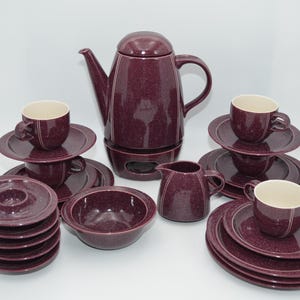 Könnte beinhalten: Ein Set aus purpurfarbenen, gesprenkelten Keramik-Teetassen, Untertassen und einer Teekanne mit passendem Milchkännchen. Das Set enthält eine Zuckerdose mit Deckel.