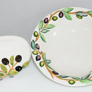 Könnte beinhalten: Zwei weiße Keramik-Servierschalen mit Olivenzweig-Designs. Die größere Schale hat einen breiten Rand und die kleinere Schale ist oval.