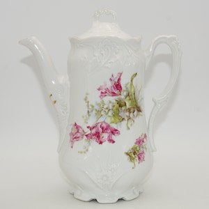 Könnte beinhalten: Weiße Porzellan-Kaffeekanne mit Deckel und Henkel. Die Kanne ist mit rosa und grünen Blumenmustern verziert. Ausguss und Henkel weisen aufwendige Details auf. Die Kanne ist etwa 25 cm hoch.