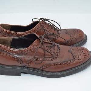 May include: A pair of brown leather brogue shoes with lace-up closures. The shoes have a wingtip design and a perforated pattern.