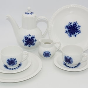 Op de afbeelding: Een wit porseleinen theeservies met een blauw sneeuwvlokkenontwerp. De set bevat een theepot, een roomkan, twee kopjes en twee schoteltjes.
