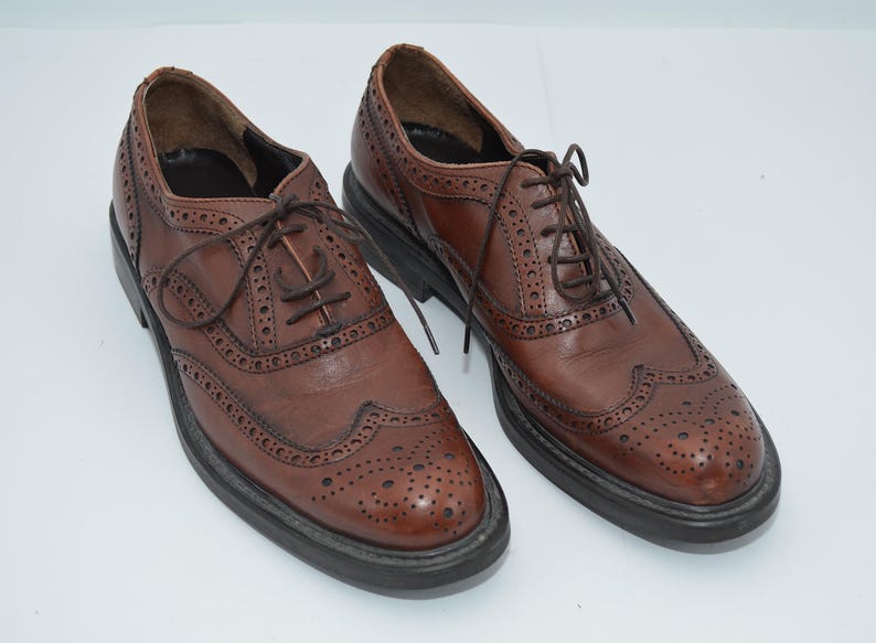 May include: A pair of brown leather brogue shoes with lace-up closures. The shoes have a wingtip design and a perforated pattern.