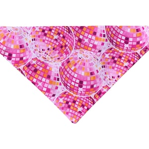 May include: A pink and white triangular pet bandana featuring a repeating pattern of disco balls. The disco balls are composed of small squares in shades of pink, orange, and white, creating a vibrant and eye-catching design.