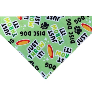 May include: A light green dog bandana with the text "Disc Dog" and "Just Throw It!" in white and black. The bandana also features images of a frisbee and paw prints.