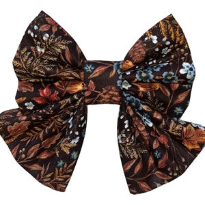 May include: A brown fabric bow with a floral pattern featuring blue, orange, and red accents. The bow is made of a soft, textured fabric and has a slightly ruffled appearance.