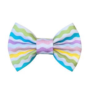 May include: A colorful bow tie with a wavy pattern in pastel shades of yellow, green, blue, and purple. The bow tie is centered on a white background, showcasing its vibrant design. This accessory is suitable for various occasions.