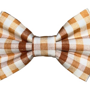 May include: A brown and white gingham bow tie. The bow tie is made of a soft, woven fabric and has a classic bow shape.
