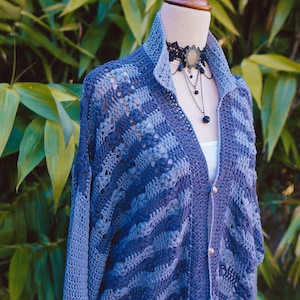 Puede incluir: Un cárdigan de crochet azul con un patrón a rayas y un delicado collar de encaje con un colgante negro.