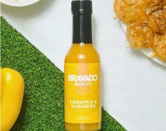 May include: A yellow bottle of hot sauce with a black label that reads "BRAVADO Spice Co." and "Pineapple & Habanero Hot Sauce" with a medium heat rating.