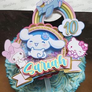 May include: A vibrant cake topper with cartoon characters, a rainbow, and the name "Sariah". The topper includes a blue aeroplane, a cloud with the number 10, and Hello Kitty and My Melody. The cake has blue frosting.