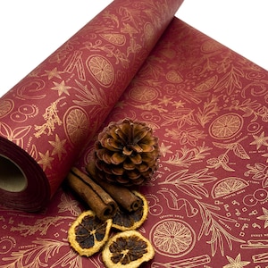 May include: Red wrapping paper with a gold foil design of spices, citrus fruits, and leaves. The paper is rolled up and there are cinnamon sticks, dried orange slices, and a pine cone on top of it.