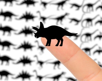 May include: A sheet of stickers with black silhouette images of dinosaurs. A finger is holding a sticker of a black triceratops dinosaur.