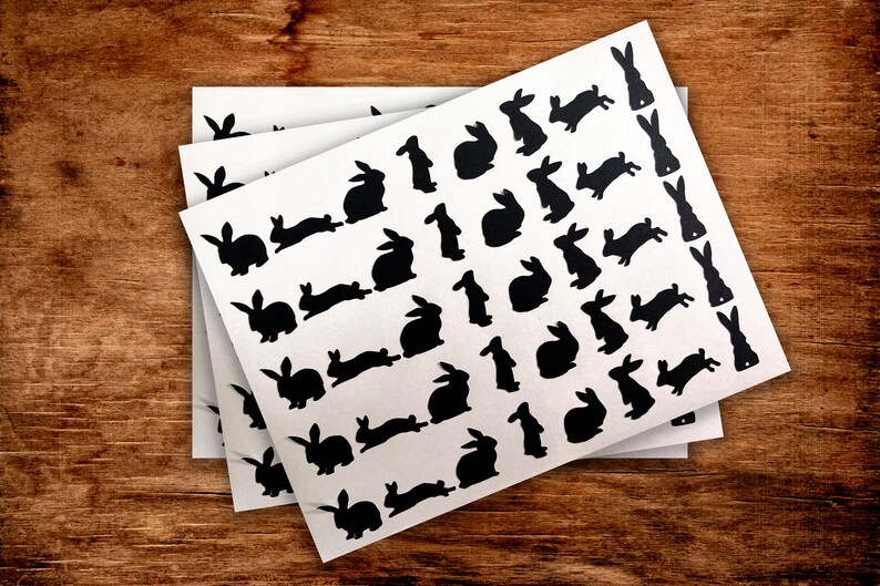 Puede incluir: Tres hojas de papel blanco con pegatinas de conejos de silueta negra. Las pegatinas son de varios tama&ntilde;os y poses.