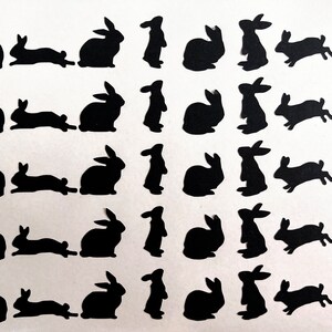 Puede incluir: Una hoja de papel negro con 20 siluetas de conejos recortadas. Los conejos est&aacute;n en varias poses, incluyendo de pie, sentados y saltando.